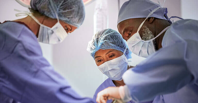 A imagem mostra uma equipe de profissionais em uma sala cirúrgica. 